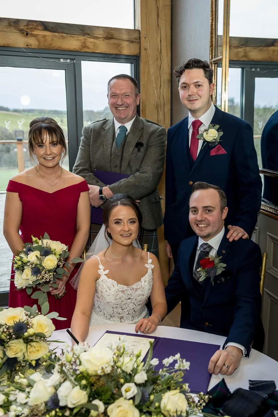 Bride, groom, witnesses and celebrant smile for a picture whilst signing marriage certificate
